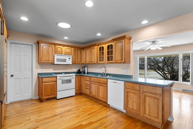 kitchen with a sink, dark countertops, white appliances, brown cabinetry, and light wood finished floors