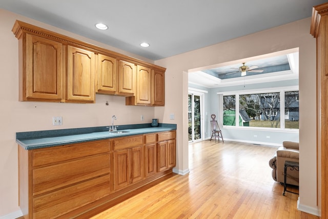 kitchen with light wood-style flooring, recessed lighting, ceiling fan, a sink, and a raised ceiling