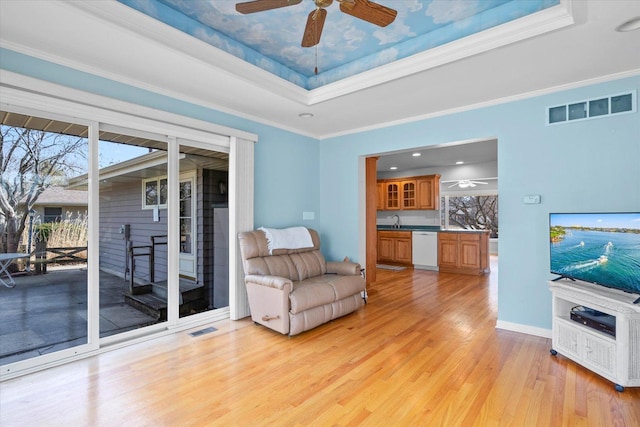 living room with visible vents, ornamental molding, light wood-style flooring, a tray ceiling, and ceiling fan