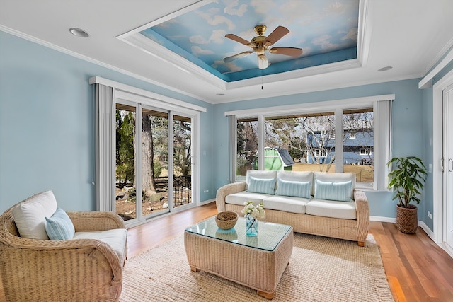 living area featuring baseboards, ceiling fan, ornamental molding, light wood-style flooring, and a raised ceiling