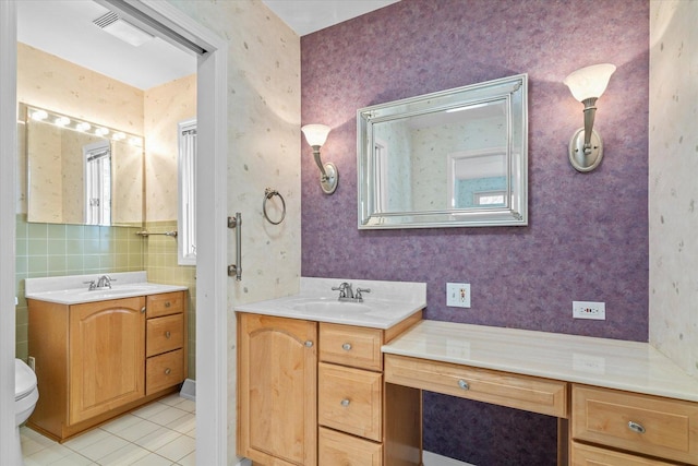 full bath featuring tile patterned floors, toilet, two vanities, a sink, and wallpapered walls