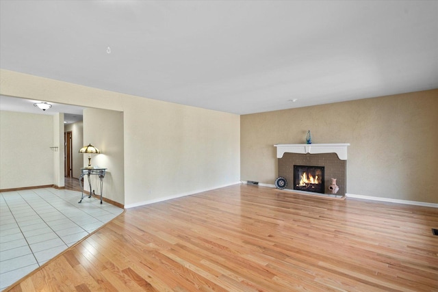 unfurnished living room featuring a brick fireplace, wood finished floors, and baseboards