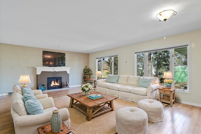 living area featuring baseboards, a brick fireplace, and wood finished floors