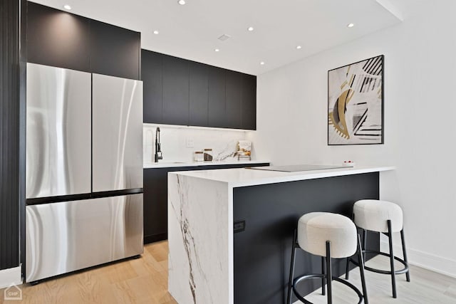 kitchen featuring a breakfast bar area, light countertops, freestanding refrigerator, modern cabinets, and dark cabinetry