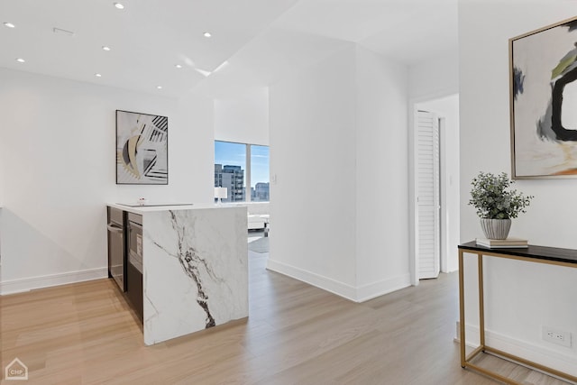 hall featuring light wood-type flooring, a view of city, baseboards, and recessed lighting