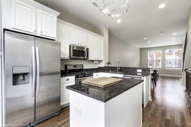 kitchen with stainless steel appliances, a peninsula, dark wood finished floors, and white cabinets