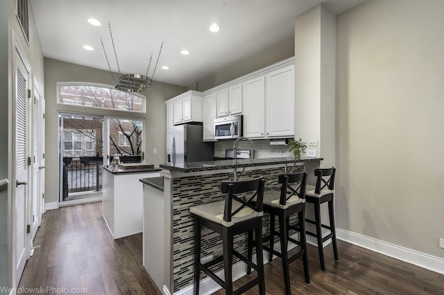 kitchen with dark countertops, appliances with stainless steel finishes, dark wood-type flooring, a peninsula, and backsplash