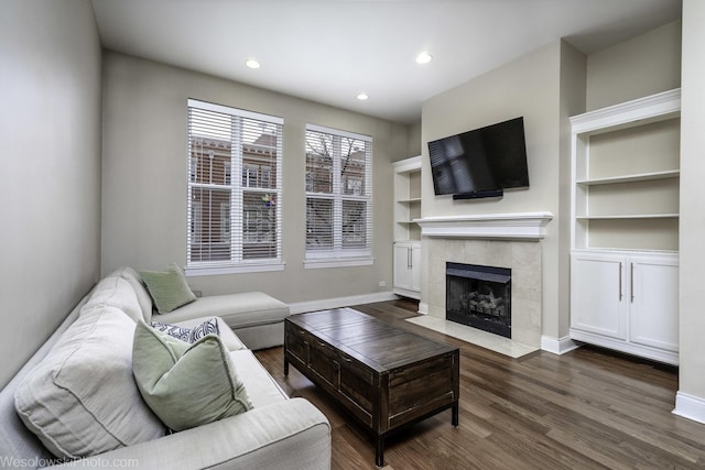 living room with built in shelves, recessed lighting, wood finished floors, a tile fireplace, and baseboards