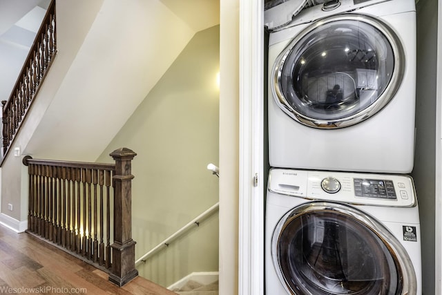 washroom featuring stacked washer and dryer, wood finished floors, and baseboards