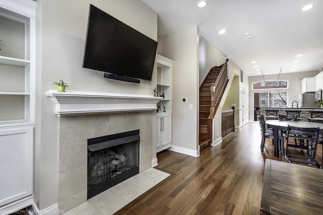 living room with built in shelves, recessed lighting, a tiled fireplace, and wood finished floors