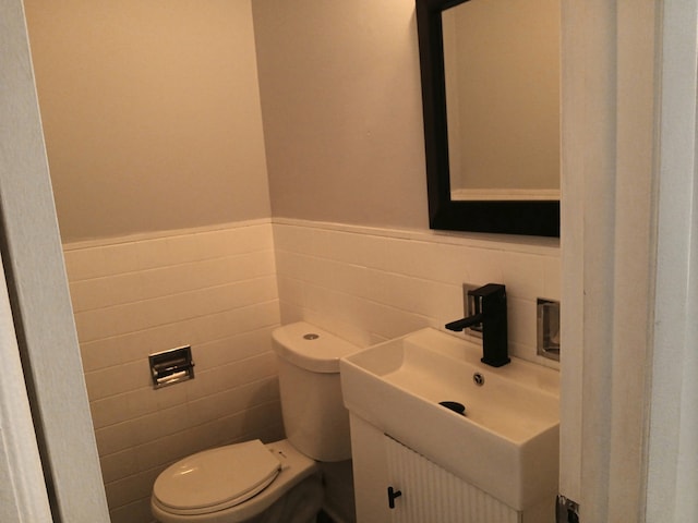 half bathroom featuring tile walls, wainscoting, vanity, and toilet