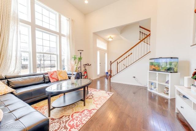 living room featuring hardwood / wood-style flooring, recessed lighting, a high ceiling, baseboards, and stairs