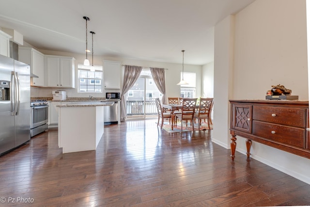 kitchen with dark wood-type flooring, a center island, white cabinetry, appliances with stainless steel finishes, and hanging light fixtures