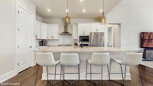 kitchen featuring a kitchen bar, dark wood-type flooring, tasteful backsplash, stainless steel appliances, and wall chimney range hood