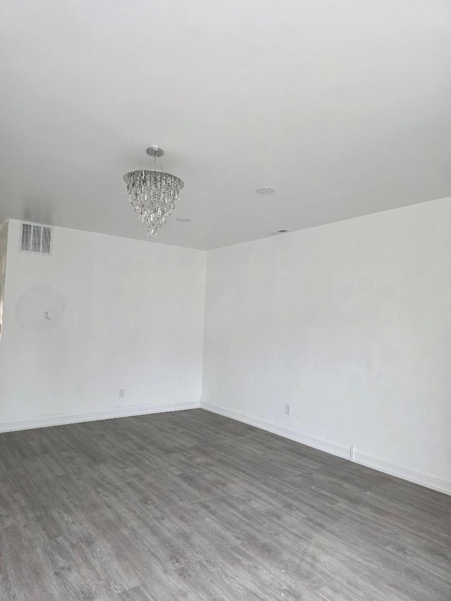 spare room featuring baseboards, wood finished floors, visible vents, and an inviting chandelier