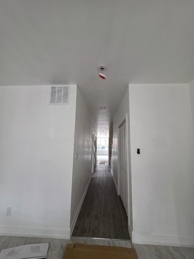 hall featuring visible vents, baseboards, and wood finished floors