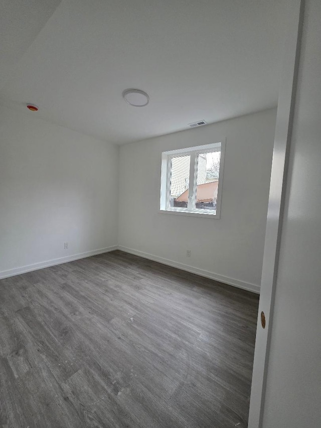 empty room featuring visible vents, baseboards, and dark wood-style flooring