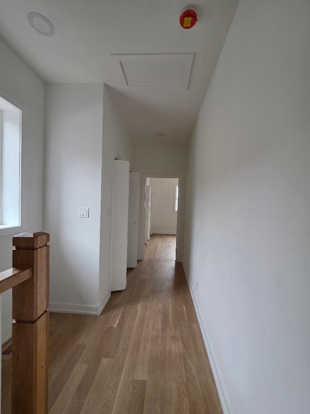 hall with light wood-style floors, attic access, and baseboards