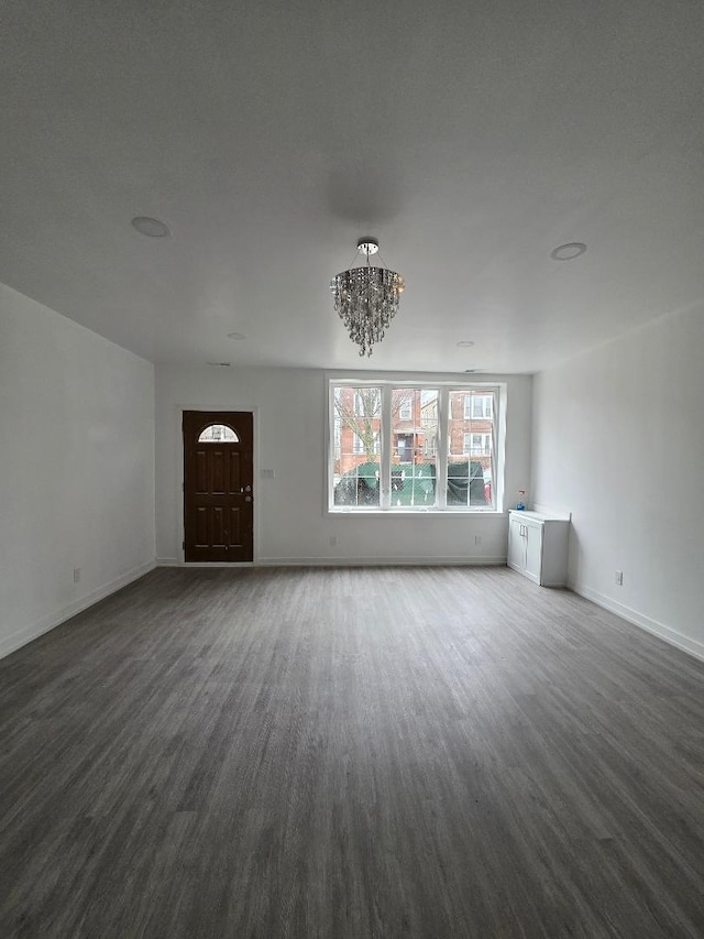 unfurnished living room with an inviting chandelier, baseboards, and dark wood-type flooring