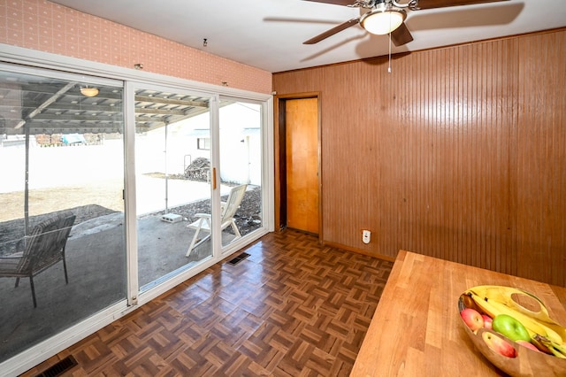 interior space with wooden walls, visible vents, baseboards, and a ceiling fan