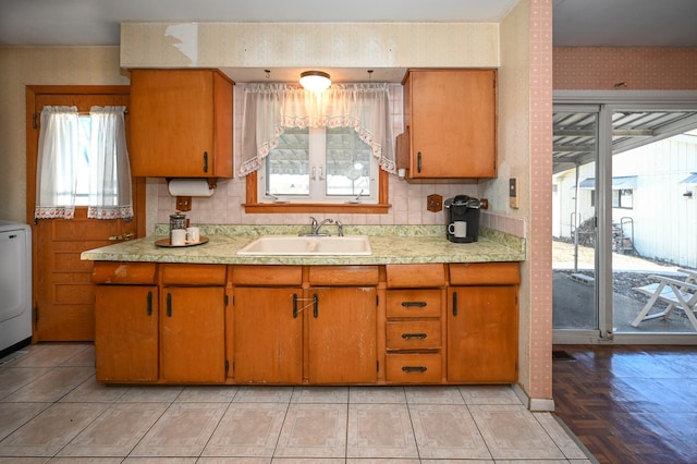 kitchen with brown cabinets, wallpapered walls, light countertops, and a sink