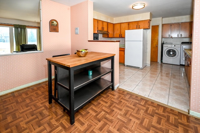 kitchen with brown cabinets, under cabinet range hood, freestanding refrigerator, separate washer and dryer, and wallpapered walls