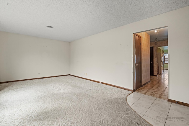 spare room featuring a textured ceiling, light carpet, and baseboards