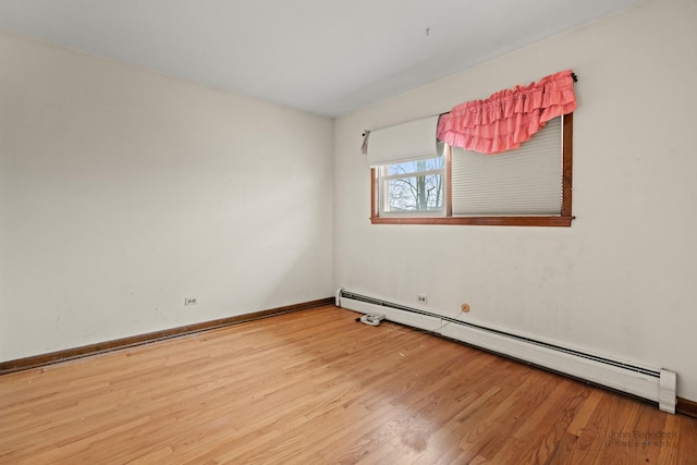 spare room featuring a baseboard heating unit, wood finished floors, and baseboards