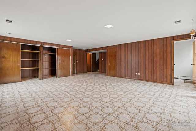 interior space with light floors, wooden walls, visible vents, and a baseboard heating unit