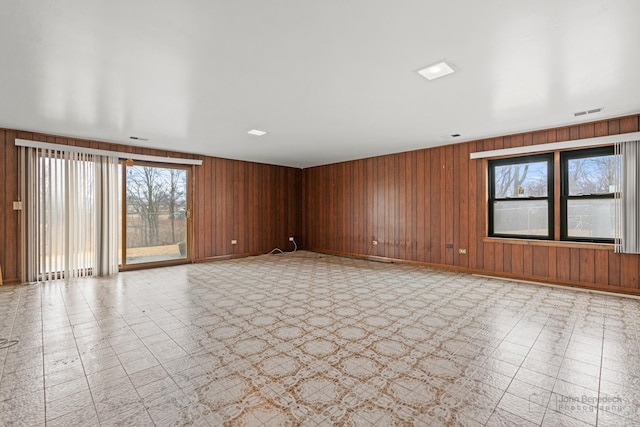 spare room featuring baseboards, wood walls, and light floors