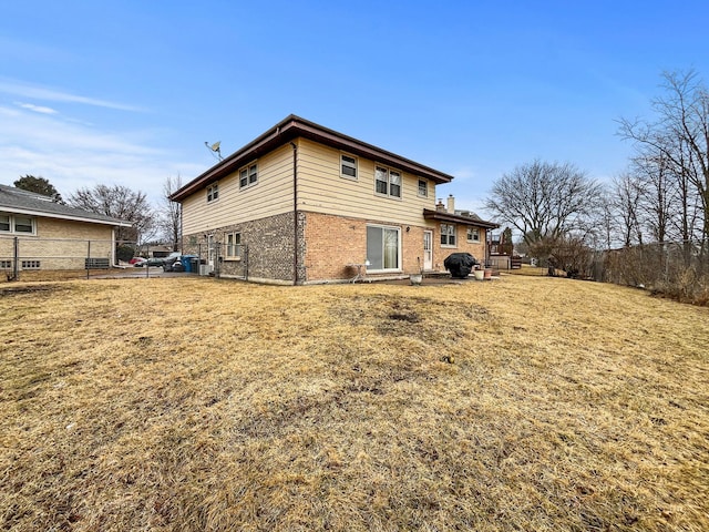 rear view of house with brick siding, a lawn, and fence