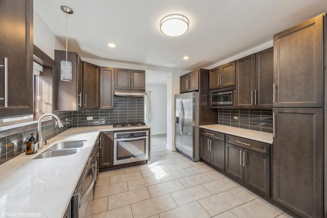 kitchen featuring light stone counters, backsplash, appliances with stainless steel finishes, a sink, and dark brown cabinetry