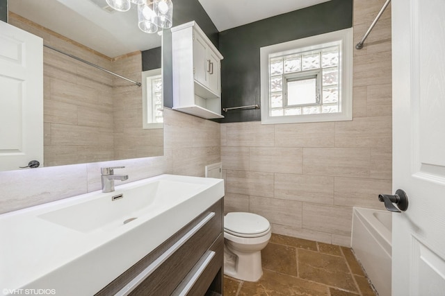 full bath featuring stone tile floors, toilet, vanity, washtub / shower combination, and tile walls