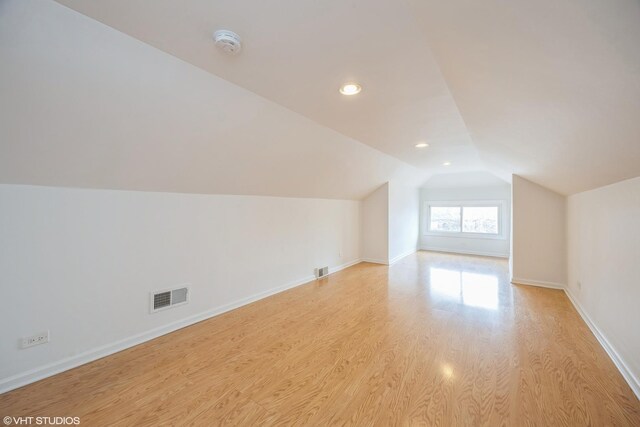 additional living space with light wood-type flooring, baseboards, visible vents, and vaulted ceiling