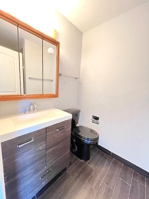 half bath featuring toilet, baseboards, wood finish floors, and vanity