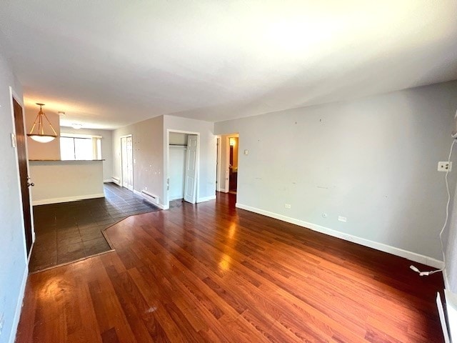 unfurnished living room featuring a baseboard heating unit, dark wood finished floors, and baseboards