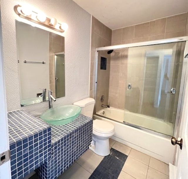 bathroom with a textured wall, tile patterned flooring, toilet, shower / bath combination with glass door, and vanity