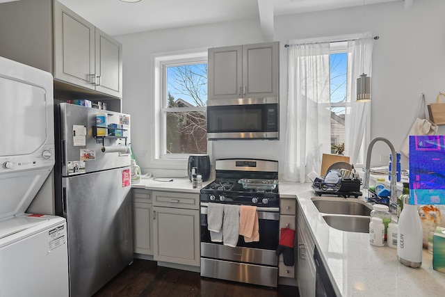 kitchen with gray cabinetry, stacked washer and dryer, appliances with stainless steel finishes, plenty of natural light, and a sink
