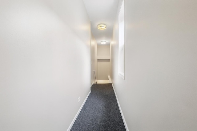 corridor featuring baseboards and dark colored carpet