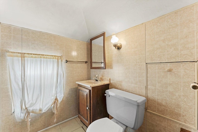 bathroom with toilet, tile patterned floors, vaulted ceiling, vanity, and tile walls