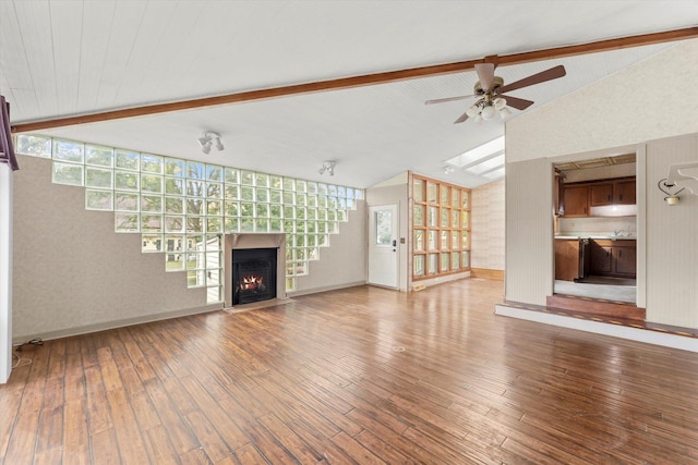 unfurnished living room with lofted ceiling with beams, ceiling fan, baseboards, a lit fireplace, and wood-type flooring