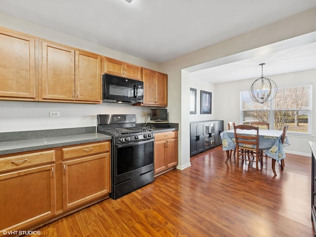 kitchen featuring dark countertops, stainless steel range with gas cooktop, black microwave, an inviting chandelier, and dark wood-style flooring