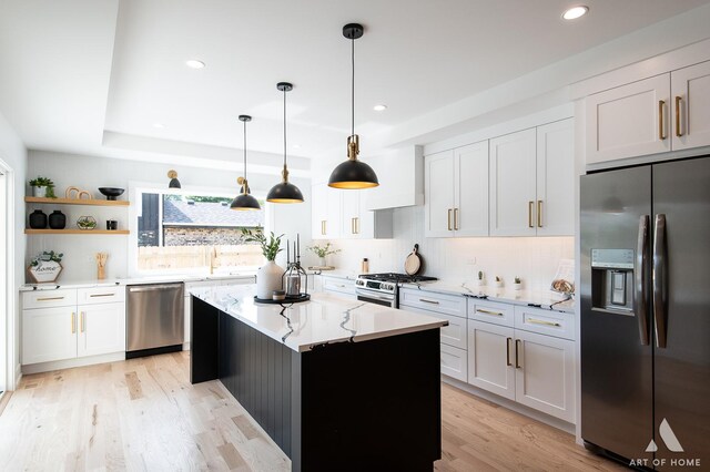 kitchen featuring light stone counters, a center island, backsplash, appliances with stainless steel finishes, and light wood-style floors