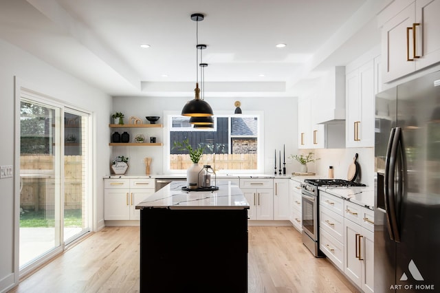 kitchen with a raised ceiling, wall chimney exhaust hood, fridge with ice dispenser, light wood-type flooring, and stainless steel range with gas cooktop