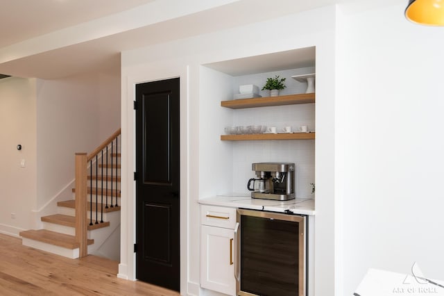 bar featuring a dry bar, light wood finished floors, beverage cooler, decorative backsplash, and stairway