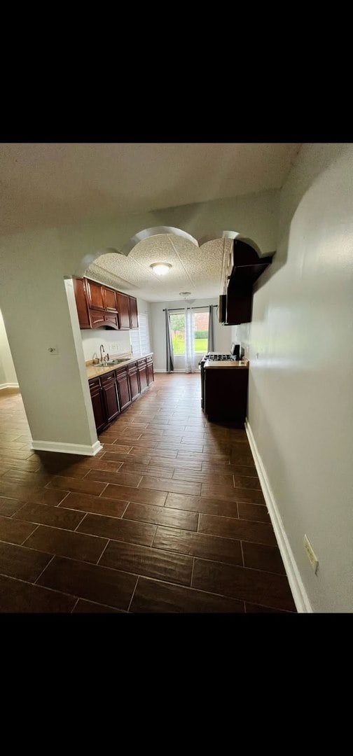 hall with baseboards, arched walkways, a textured ceiling, wood finish floors, and a sink