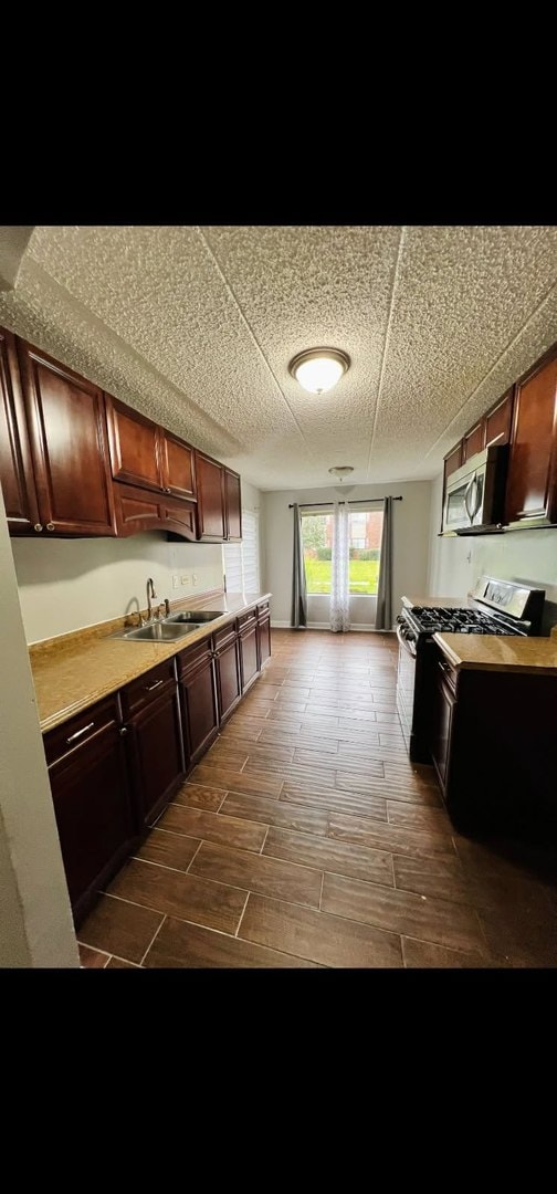 kitchen featuring wood tiled floor, stainless steel appliances, a sink, and light countertops