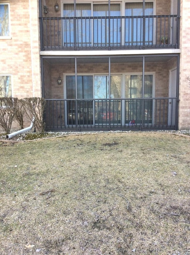 back of house with a yard, brick siding, and a balcony