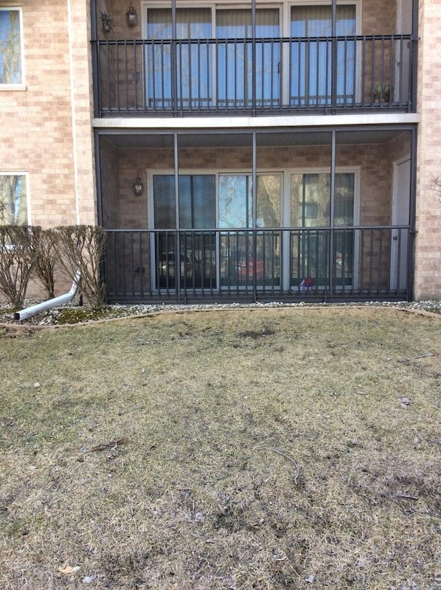 rear view of property featuring a yard, brick siding, and a balcony