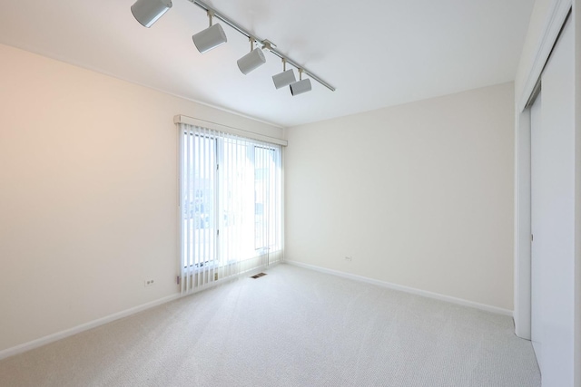 spare room with carpet flooring, rail lighting, and baseboards